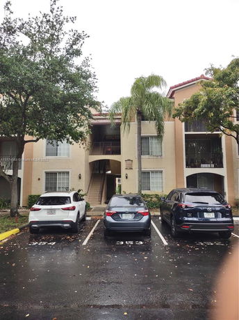 Front view of a multi-story residential building with a central stairway and adjacent parking spaces.
