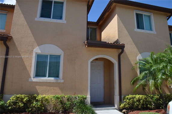 Front view of a two-story house with beige stucco walls and a white door.