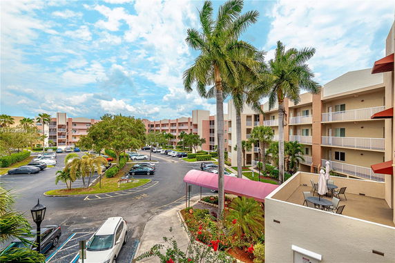 View of residential complex with palm trees and cars parked in the lot.