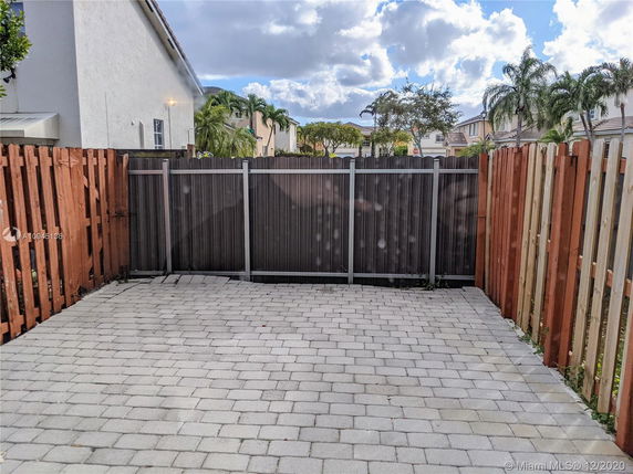 Outdoor paved area with wooden fencing and nearby houses with palm trees visible.