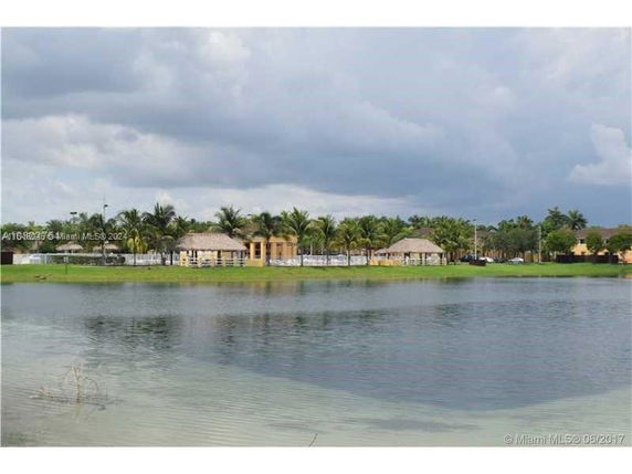 View of a lake with buildings and palm trees in the background.