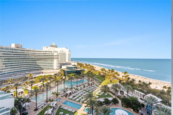 Wide angle view of a beachfront building with a pool area and palm trees.