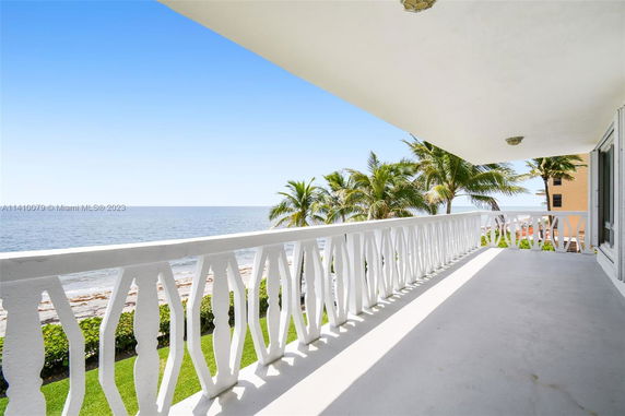 Balcony with white railing overlooking the ocean and palm trees.