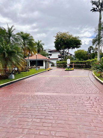 Driveway leading to a building with a small guardhouse and tropical landscaping.