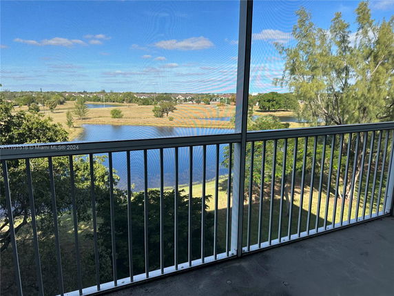 Balcony view overlooking a grassy area with a pond and trees.