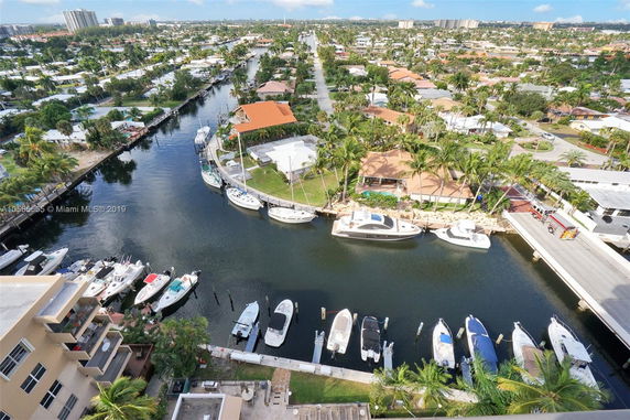 Aerial view of a waterfront neighborhood with boats docked along a canal and houses with palm trees.