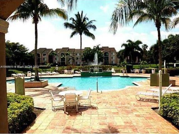 Outdoor swimming pool area with surrounding palm trees and apartment buildings in the background.