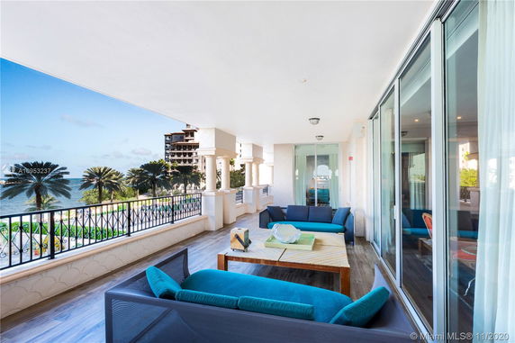 Covered outdoor balcony area with seating, overlooking a scenic view of palm trees and the sea.
