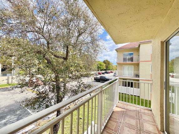 View from a balcony showing surrounding area with adjacent residential building and tree.