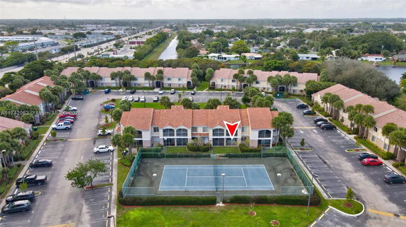 Aerial view of a residential complex with multiple two-story buildings, tennis court, and parking spaces.