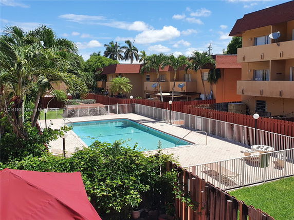 Outdoor swimming pool with nearby buildings and palm trees.