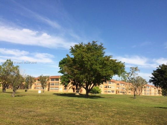 View of multiple apartment buildings with a large grassy area and trees in the foreground.