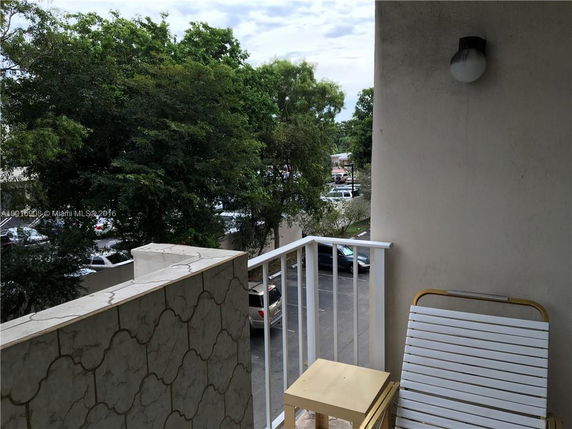 Balcony view showing surrounding trees and parked cars.