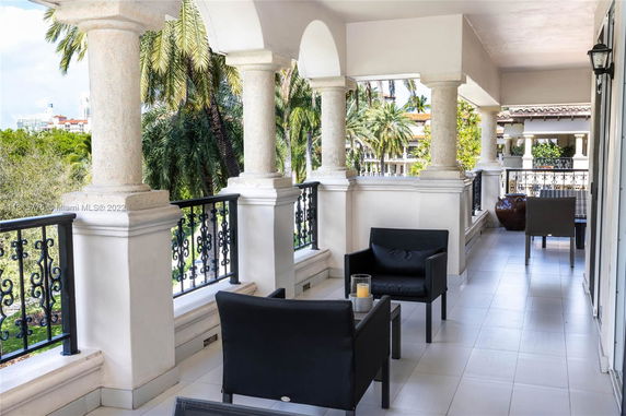 Outdoor balcony with columns and black seating, offering a view of surrounding greenery and distant buildings.