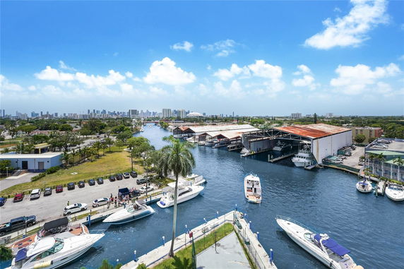 Panoramic view of a waterway with boats, surrounded by warehouses and distant city skyline.