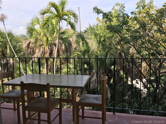 View of a balcony with a table and chairs overlooking lush greenery.