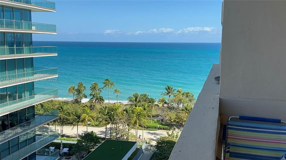 View of the ocean from a high-rise building, with palm trees in the foreground and a beach visible along the coastline.
