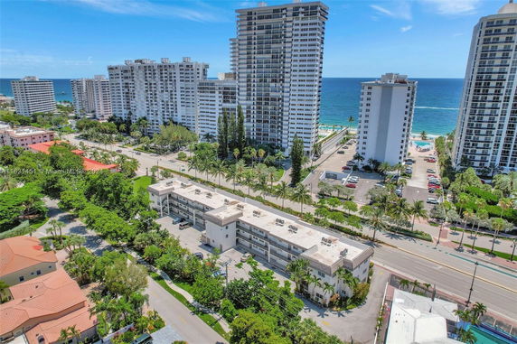 Aerial view of high-rise residential buildings near a coastline, with a road and greenery in the foreground.