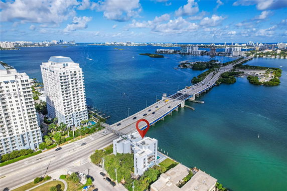 Aerial view of a coastal area with several residential buildings near a bridge over water.