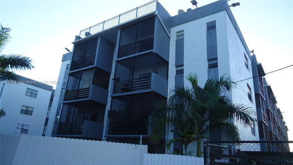 Front view of a multi-story building with balconies and a rooftop railing.