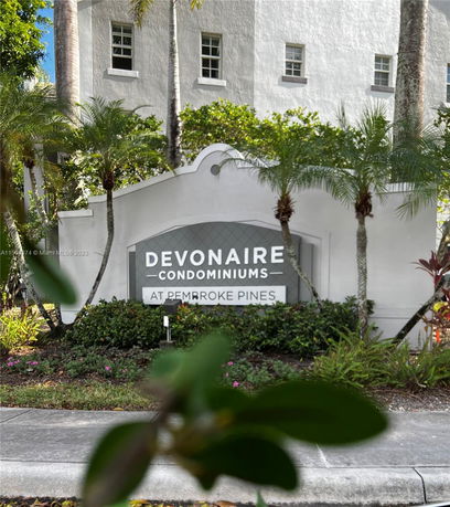 Front view of a condominium sign with a white building in the background.