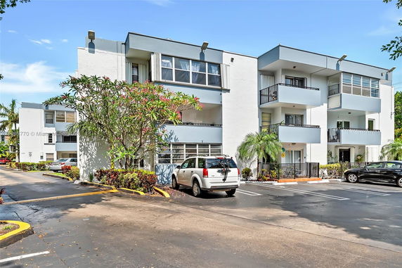 Front view of a modern three-story building with balconies and parking area.