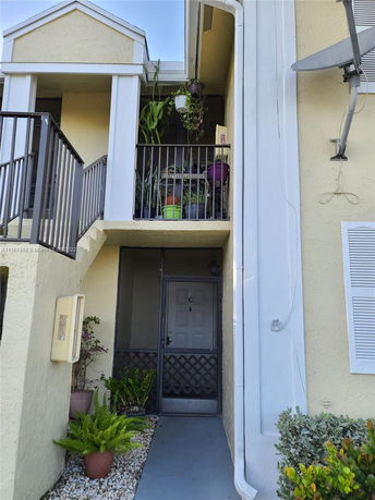Front view of a two-story building entrance with plants on the balcony.