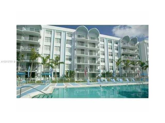 Front view of a multi-story building with balconies and a swimming pool in front.