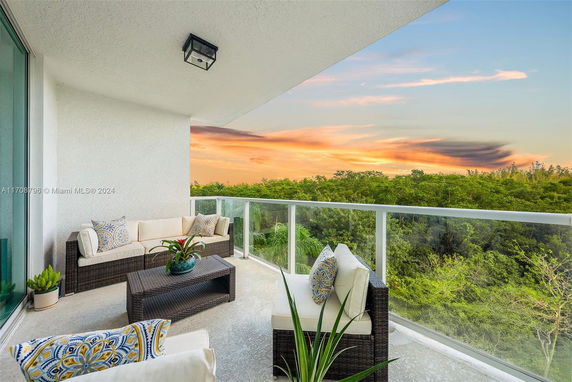 Balcony with outdoor seating and scenic view of trees at sunset