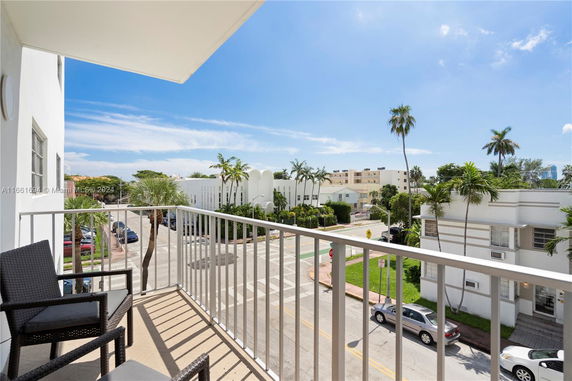 View from a balcony overlooking a street with palm trees and several buildings.