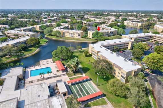 Aerial view of multiple apartment buildings surrounding a small lake, with a swimming pool and tennis courts visible in the foreground.