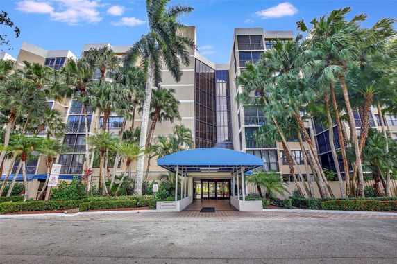 Front view of a multi-story building with a blue entrance canopy and palm trees.