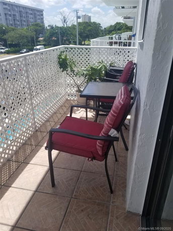 Balcony with red-cushioned chairs overlooking surrounding buildings and trees.