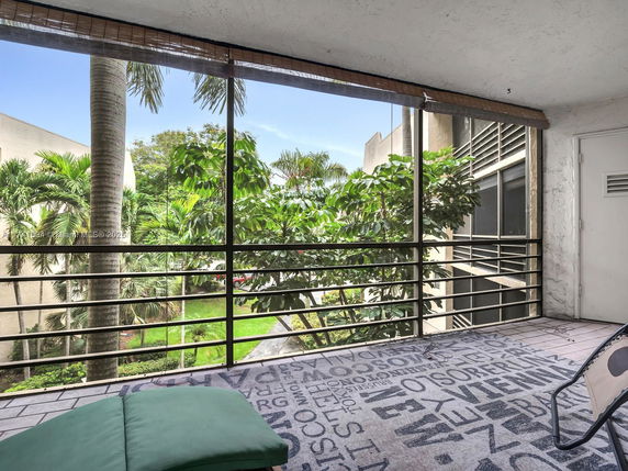 View from a balcony overlooking a green area with palm trees.