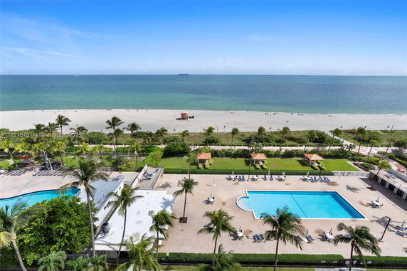 View of a swimming pool and beach area from a high vantage point overlooking the ocean.