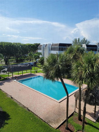 Outdoor swimming pool with surrounding palm trees and a nearby building.