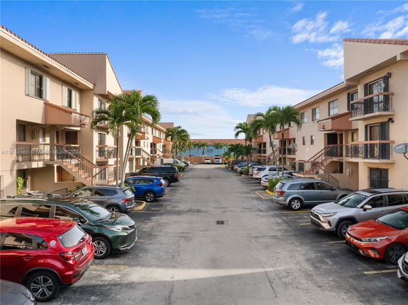 Outdoor parking area with cars in front of apartment buildings.