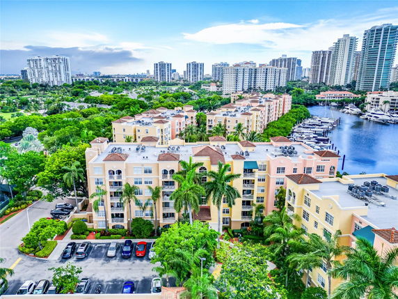 Aerial view of residential buildings near a marina with yachts and greenery in a cityscape.