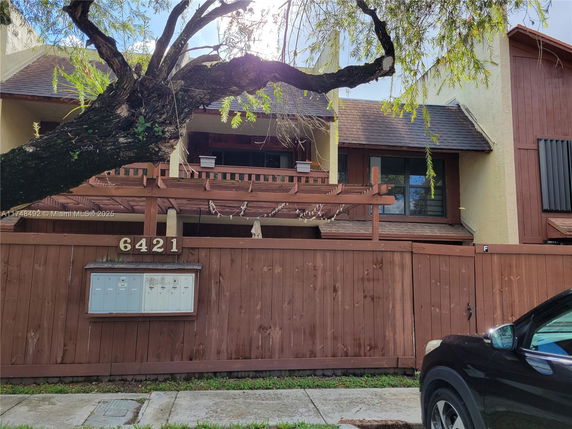 Front view of a two-story house with wooden fencing and a pergola.