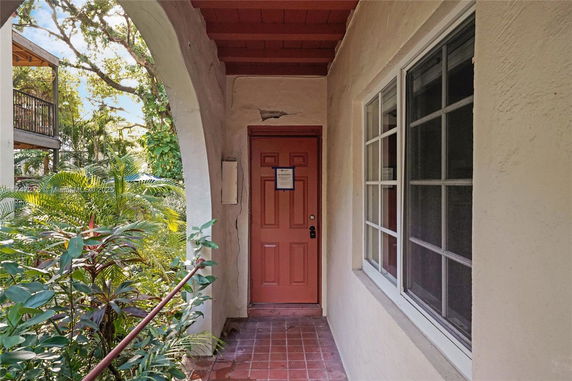 Front view of a house entrance with an arched doorway and red door.