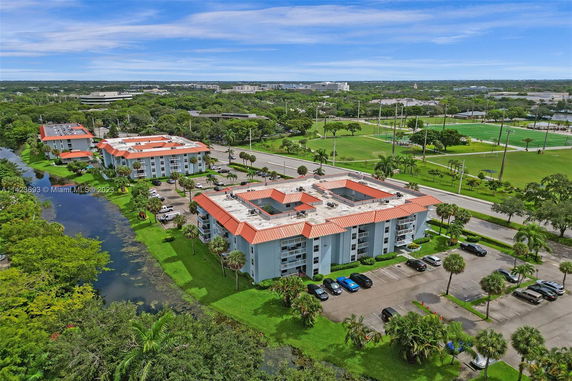 Aerial view of multiple residential buildings with red roofs, surrounded by greenery and a waterway.