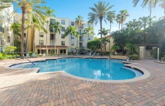 Outdoor swimming pool in front of a multi-story building with palm trees.