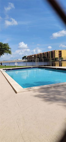 Outdoor swimming pool with surrounding view of multi-story buildings and a water body.