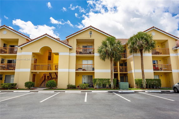 Front view of a multi-story apartment building with balconies and parking area.