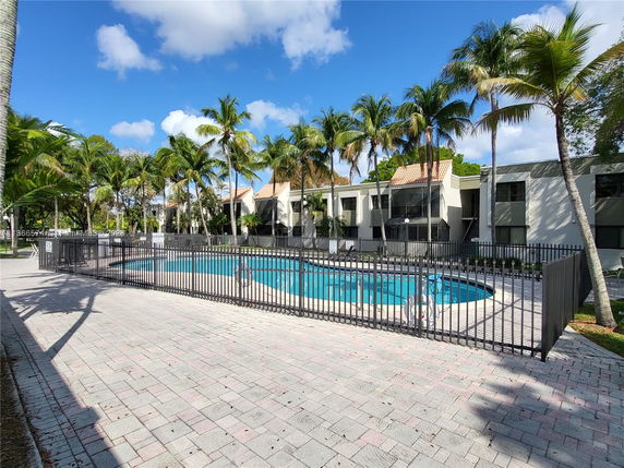 Outdoor swimming pool area with surrounding fence and nearby buildings.