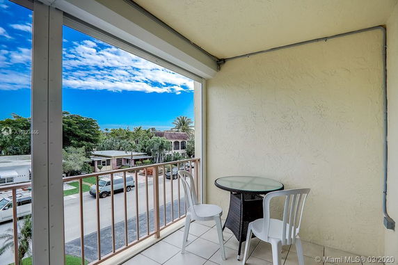 Balcony view with table and chairs overlooking a neighborhood scene with houses and trees.