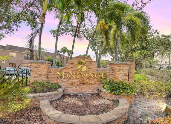 Front view of a residential complex entrance with stone signage and tropical landscaping.