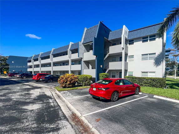 Front view of a multi-story apartment building with visible parking spaces.