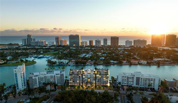 Panoramic view of cityscape with tall buildings and water in the foreground during sunset.