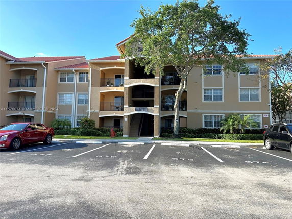 Front view of a three-story apartment building with balconies and a parking area.